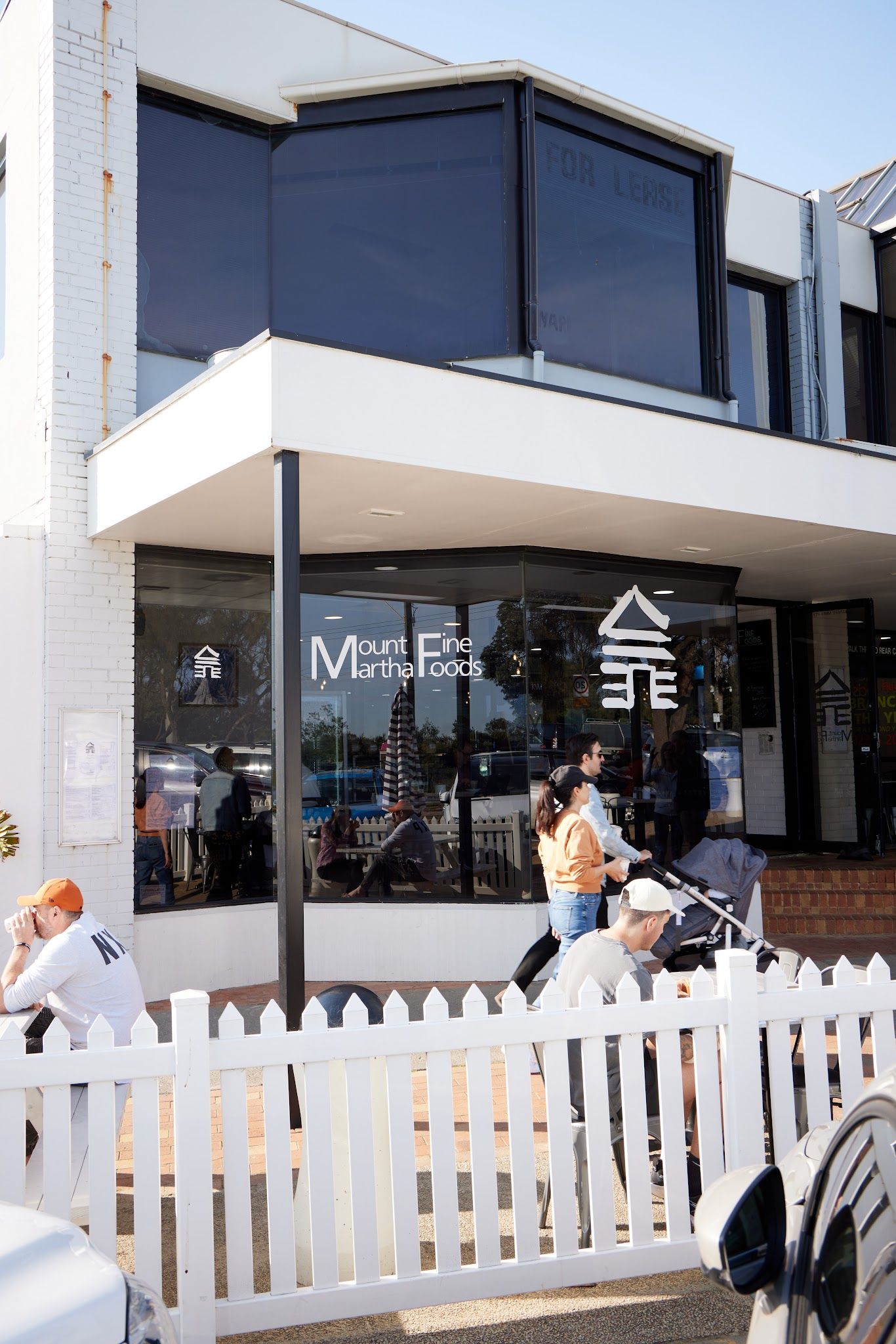 Mount Martha Fine Foods exterior — white shopfront with black trim, white picket fence, customers outside