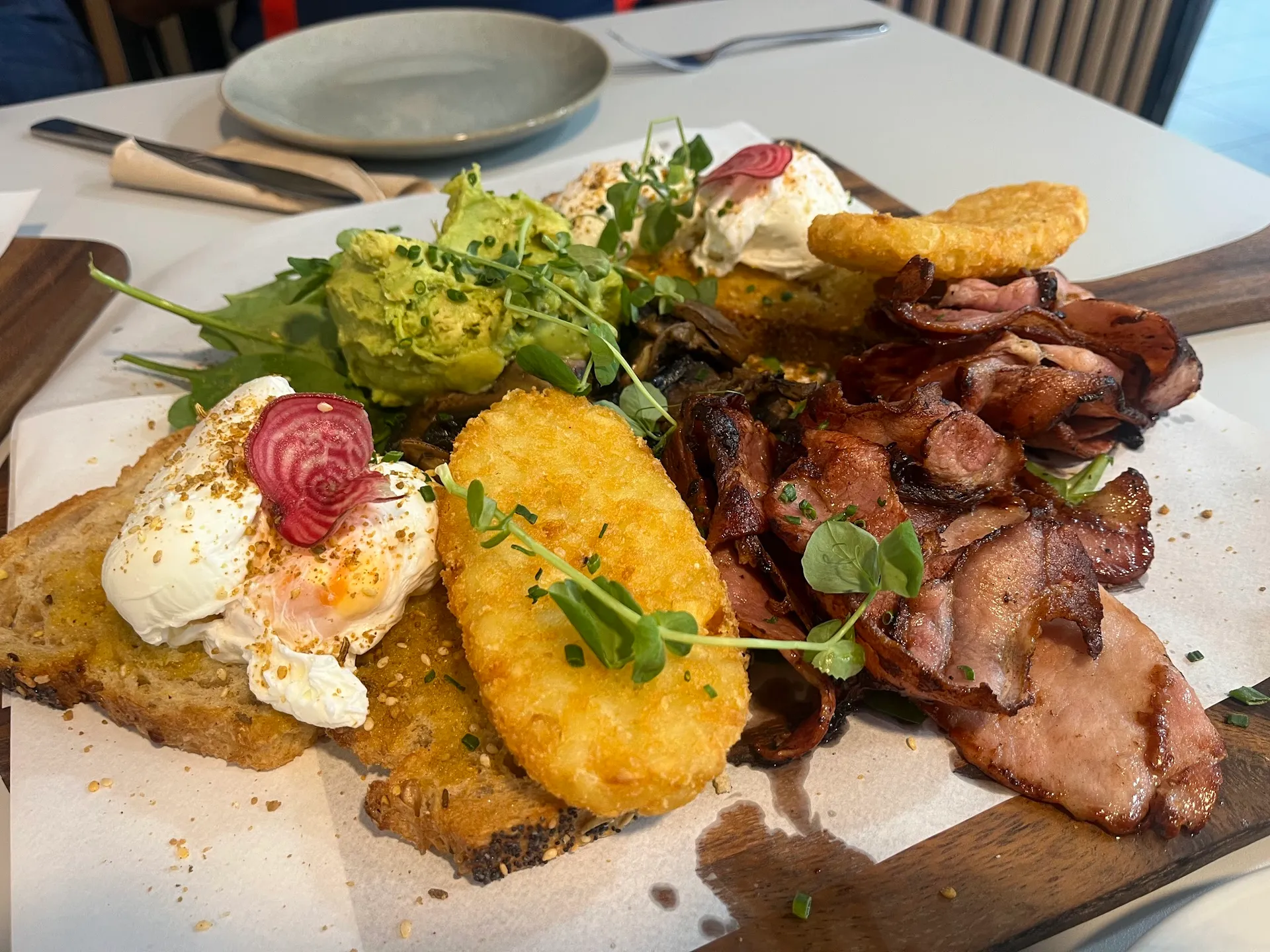 Big breakfast board with poached eggs, avocado, bacon, hash brown and microgreens on sourdough