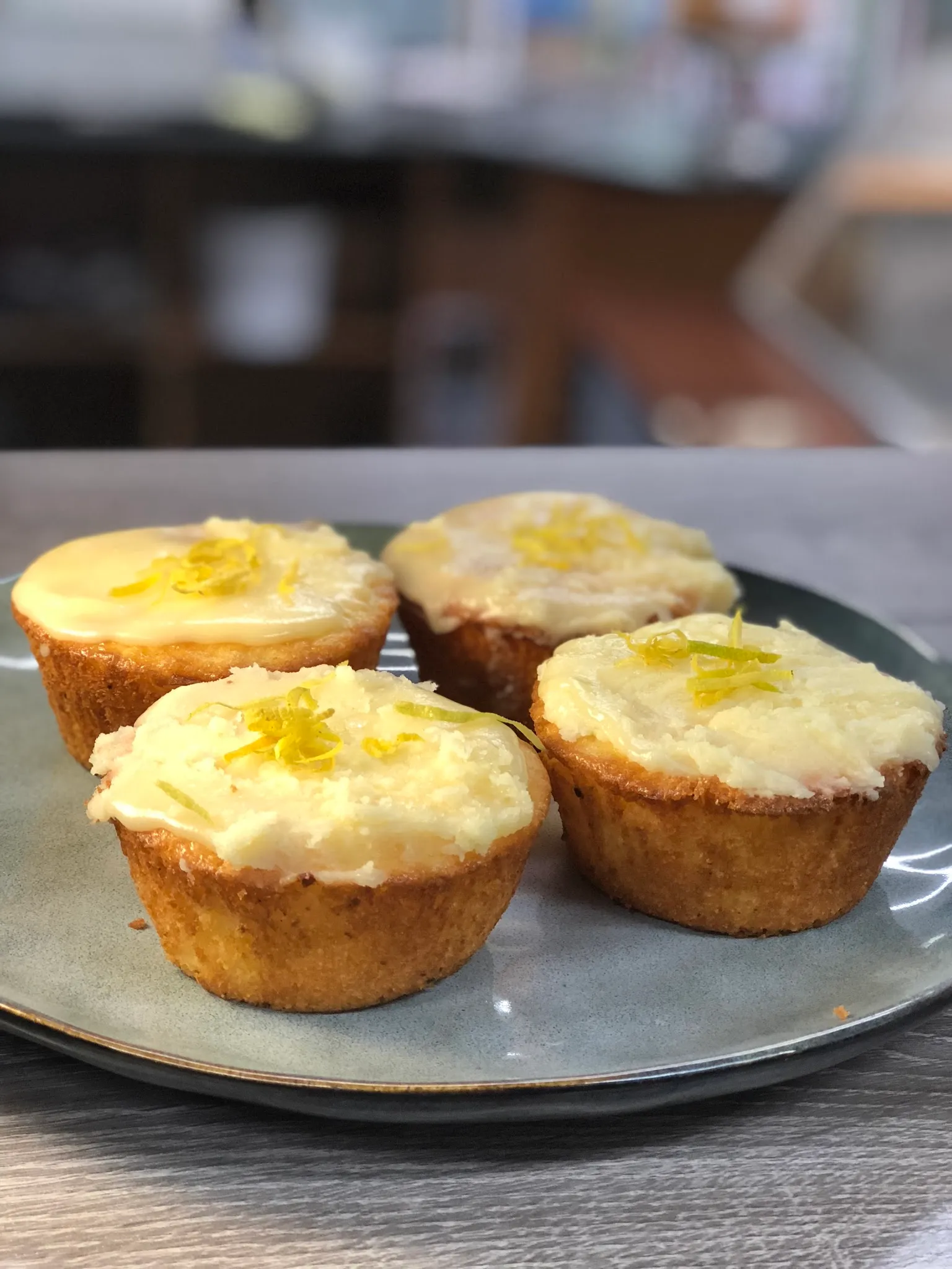 Four lemon friands with cream glaze and candied lemon zest on a sage-green ceramic plate