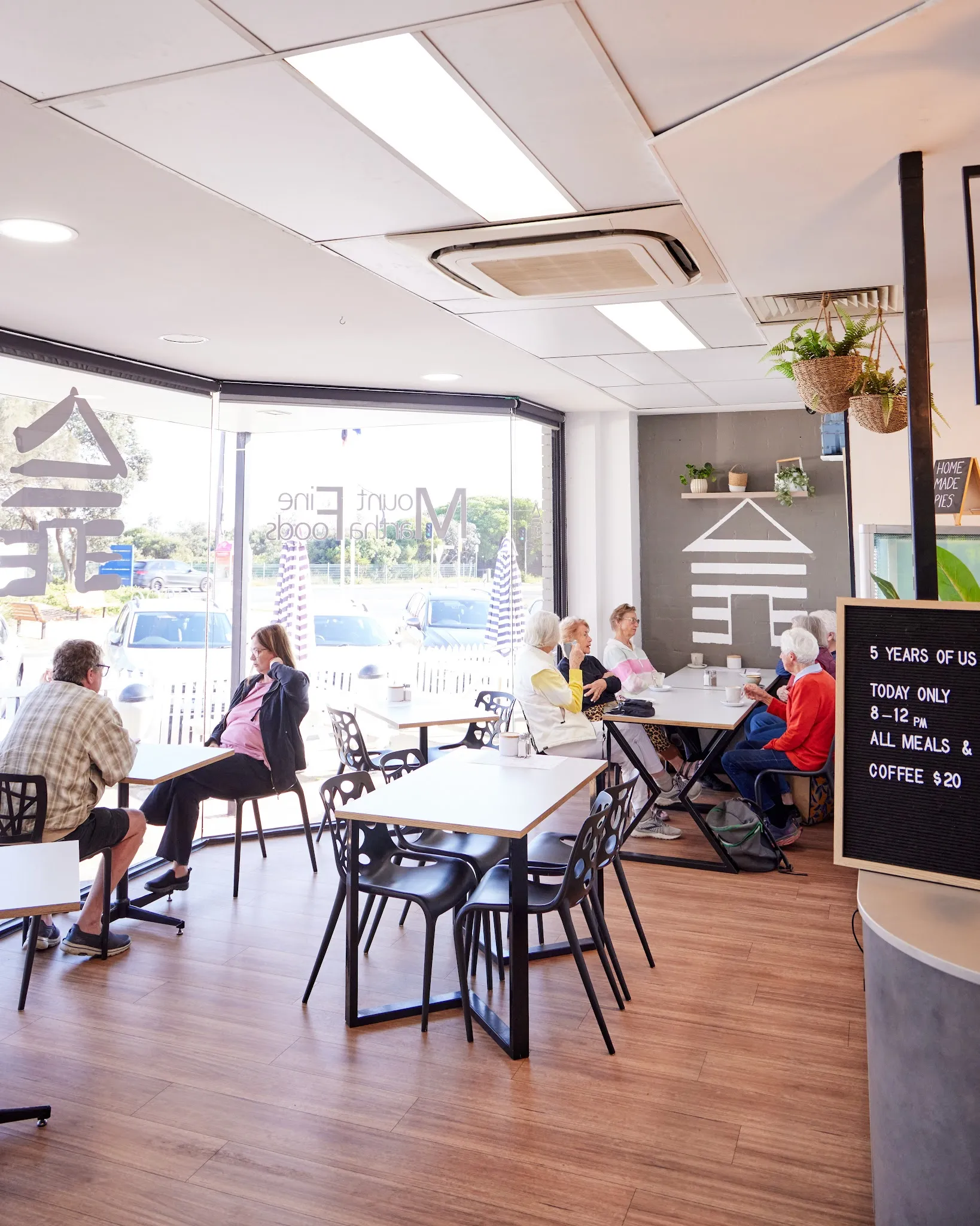 Interior dining room with customers at white tables, large windows and natural light