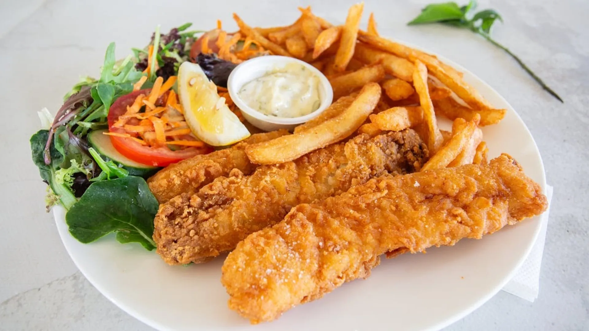 Golden crumbed fish fillets with chips, garden salad and tartare sauce on white plate
