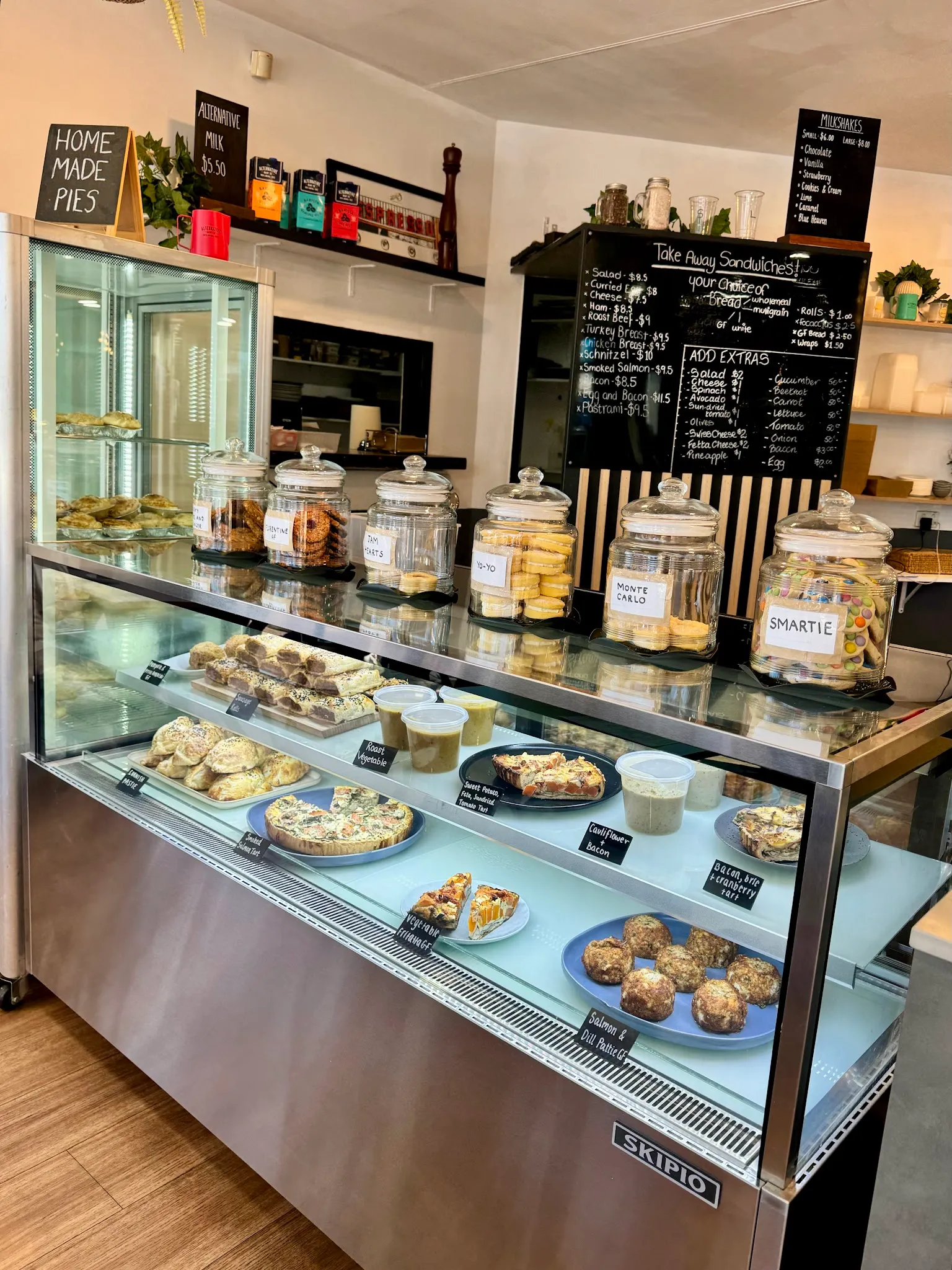 The café display cabinet stocked with pies, slices, cakes and pastries, with handwritten specials board above