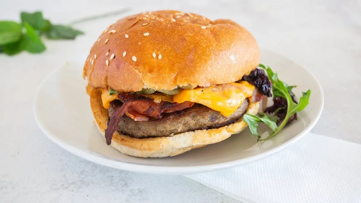 Gourmet beef burger with bacon and melted cheese on a brioche bun, white plate