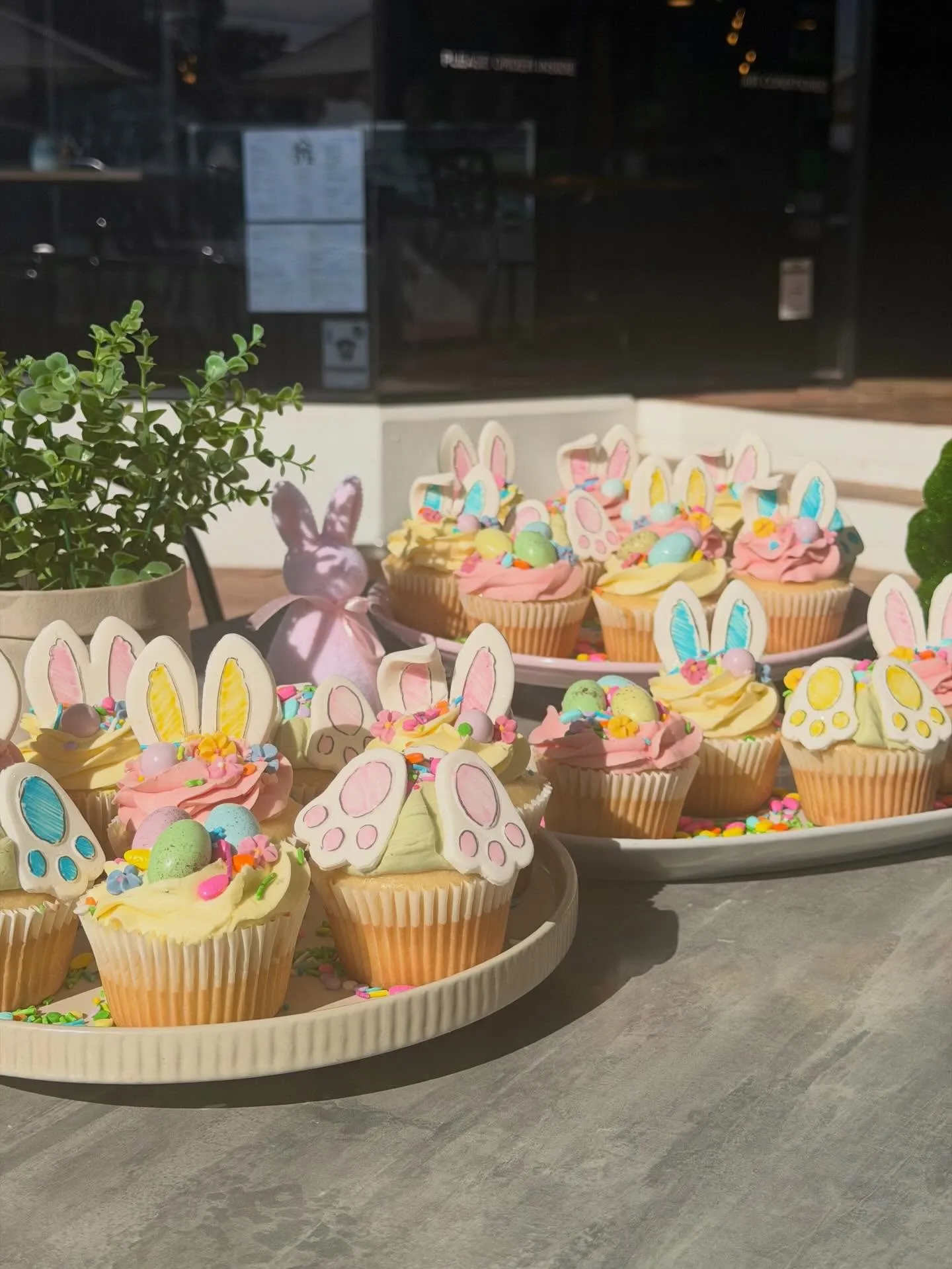 Easter cupcakes with pastel icing and bunny-ear toppers on a tiered white stand outside the café