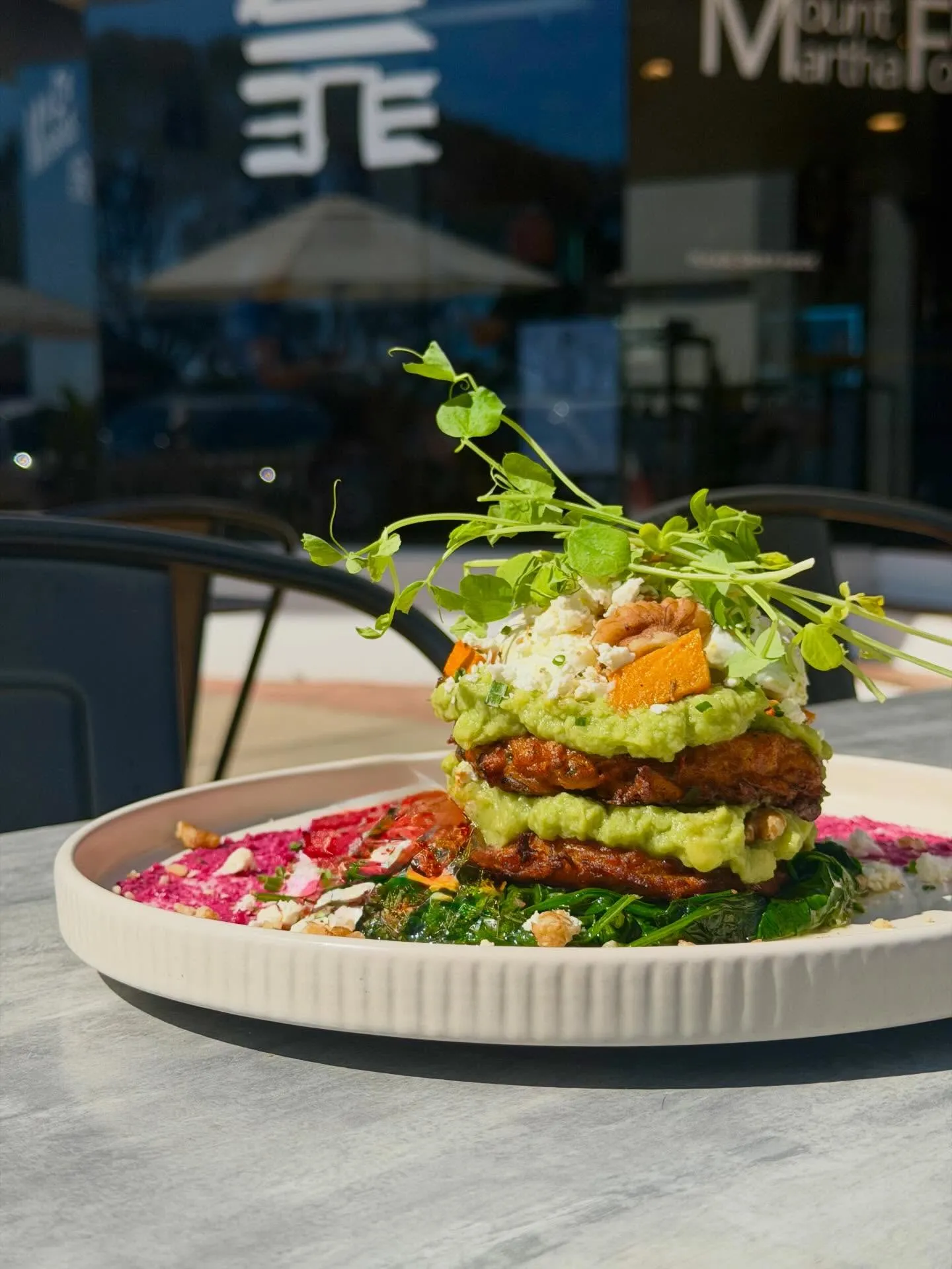 Artful stacked dish with avocado and feta at an outdoor table, shopfront visible behind